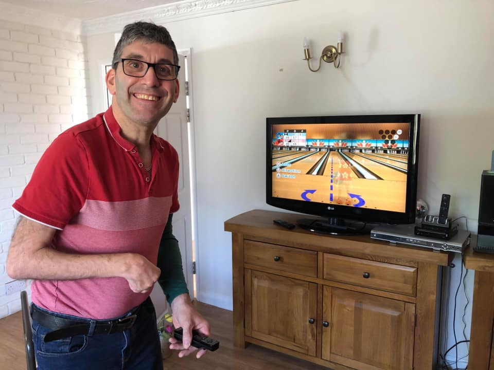 A person we support smiling at the camera, playing games on his Wii
