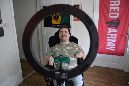 Will who has short brown hair is pictured behind the ring light he uses to film his weekly sportscasts. 