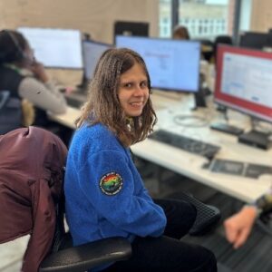 Photo of Anna, a supported intern on Royal Borough of Greenwich's Supported Internship programme. She is sat by a computer smiling at the camera